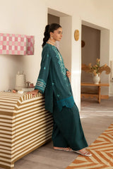 Woman in a teal traditional outfit standing in a room with a striped cabinet and decorative elements.